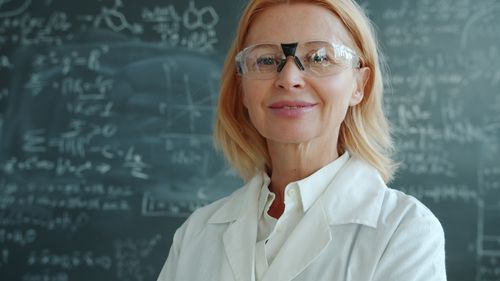 Free Smiling scientist wearing safety goggles in front of math-filled chalkboard. Stock Photo
