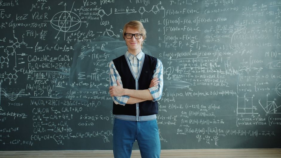 Smiling teacher stands confidently before a chalkboard filled with complex equations.