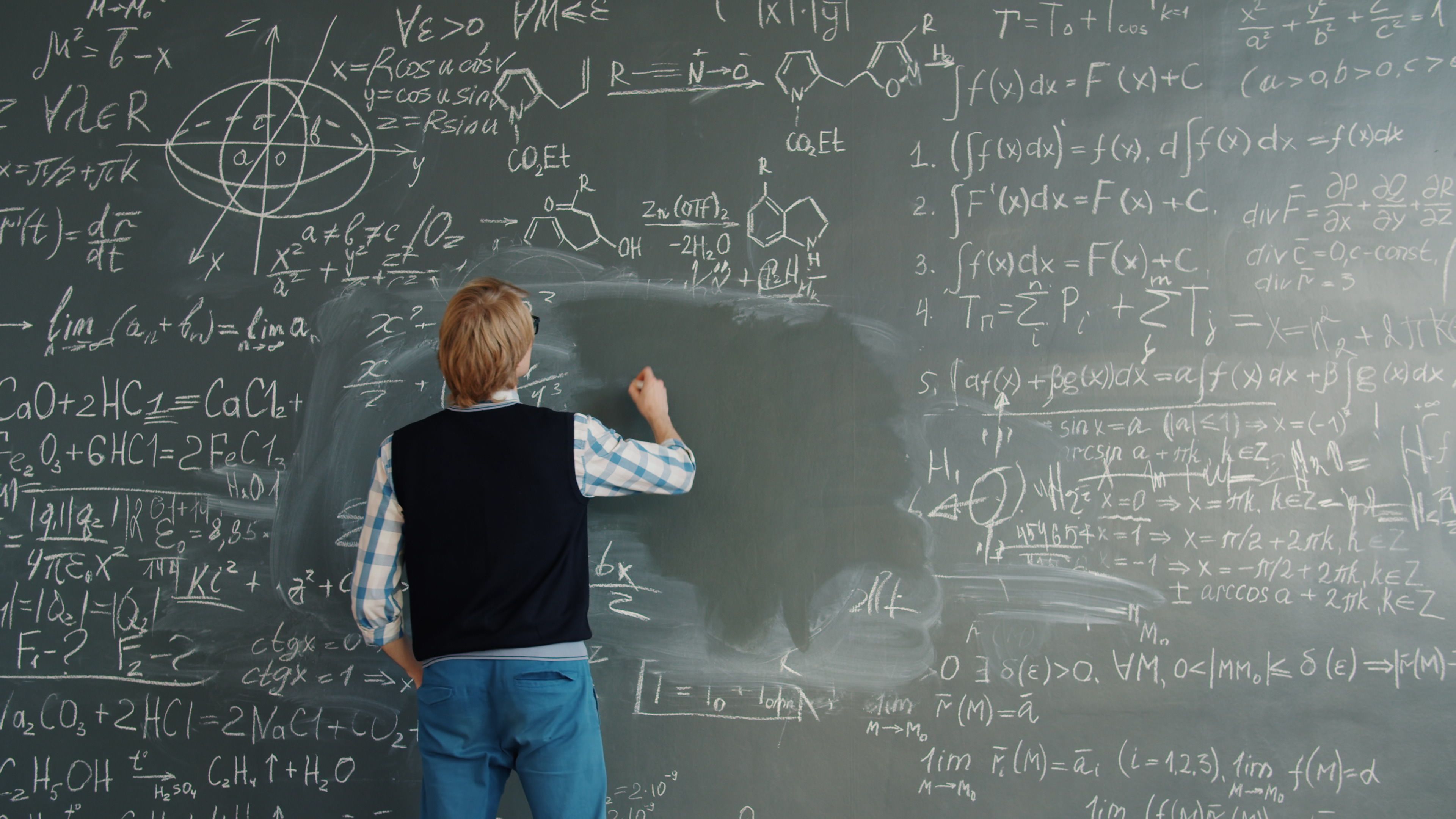 A teacher writing complex mathematical formulas on a chalkboard in a classroom.