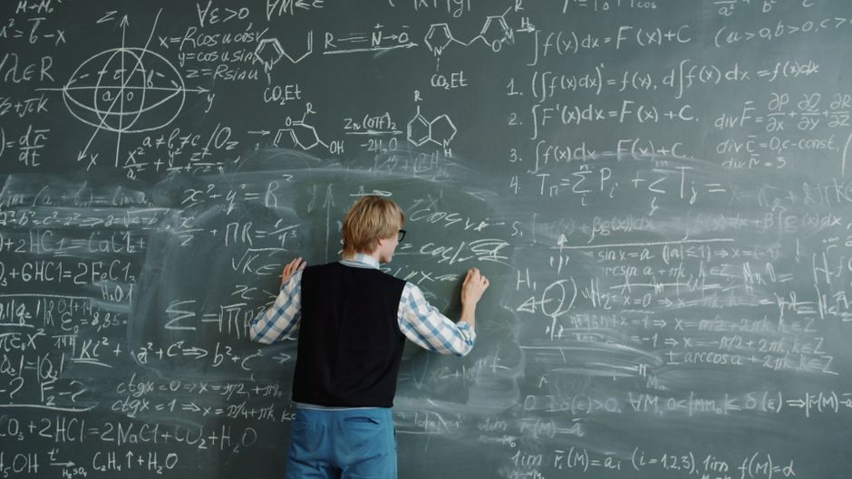 Person writing complex equations on a chalkboard, focusing on mathematics.