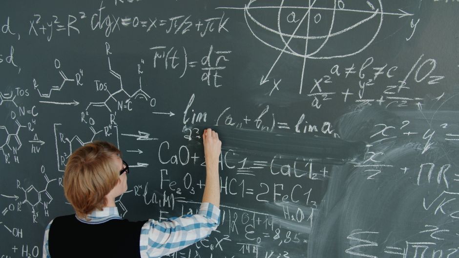Scientist or math student writing equations on a blackboard in a classroom.