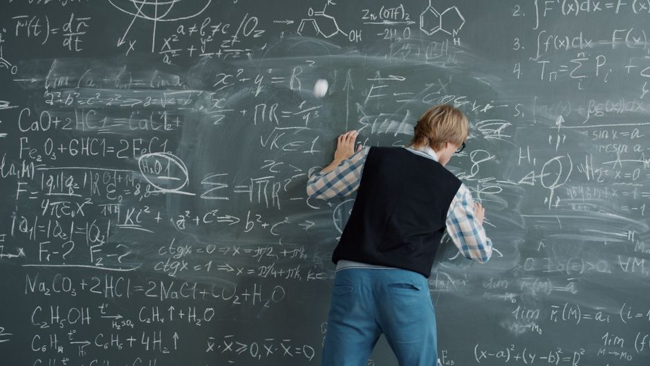 Person writing mathematical equations on a chalkboard, deep in study. Person writing mathematical equations on a chalkboard, deep in study.