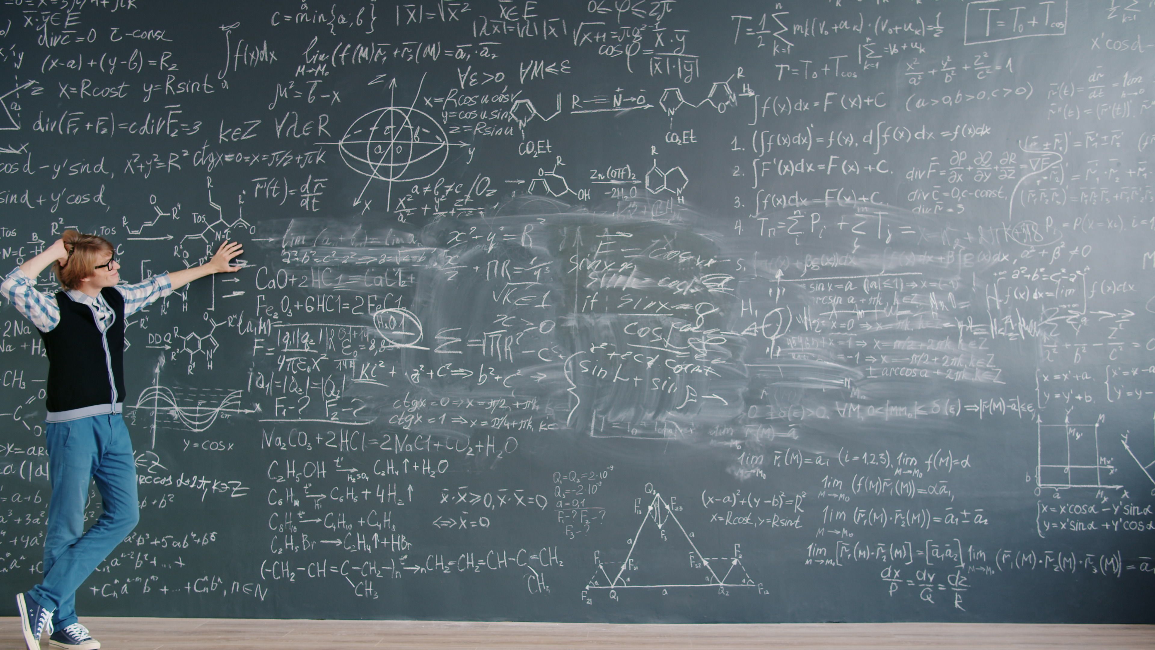 Student stands by chalkboard filled with complex math equations in a classroom setting.