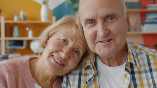 Free Charming elderly couple smiling warmly while seated indoors, enjoying a cozy moment together. Stock Photo