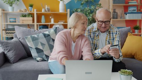Free Elderly couple using laptop and credit card in a cozy living room setting. Stock Photo