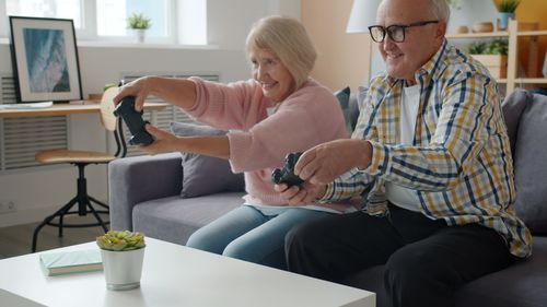 Free Happy senior couple playing video games on a couch, having fun indoors. Stock Photo