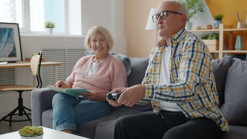 Free Elderly couple enjoying leisure time in a cozy living room with a game controller and a book. Stock Photo