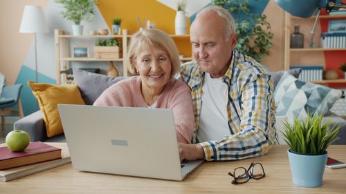 Free Elderly couple enjoying time together while browsing a laptop in a modern, cozy living room. Stock Photo