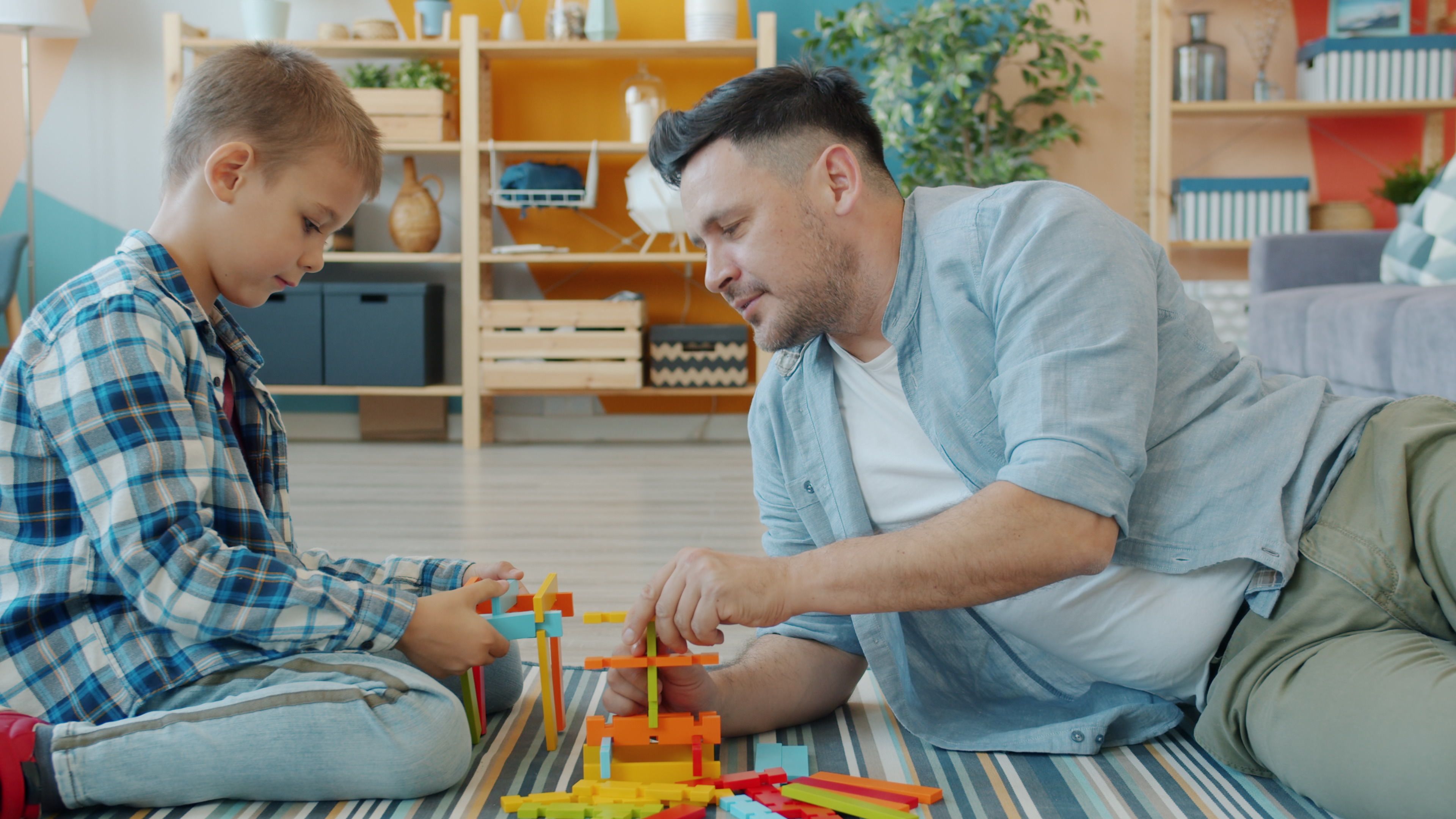 Father and son bonding while building with colorful blocks indoors.