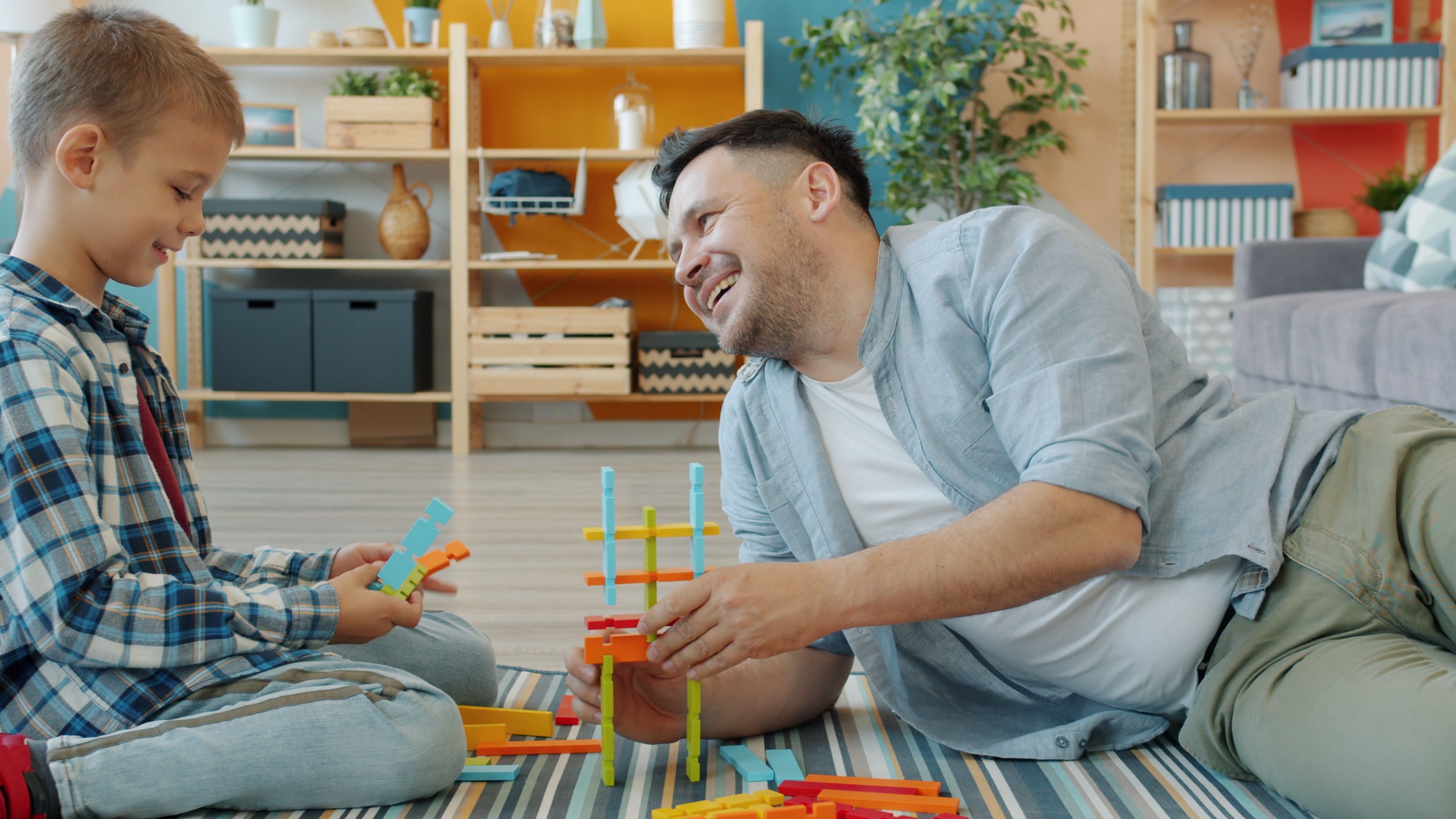 A smiling father and son playing with colorful toys indoors, fostering parent-child bonding.