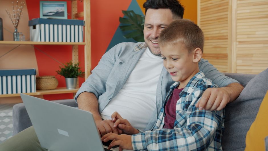 Father and son enjoying time together using a laptop at home, smiling and relaxed.