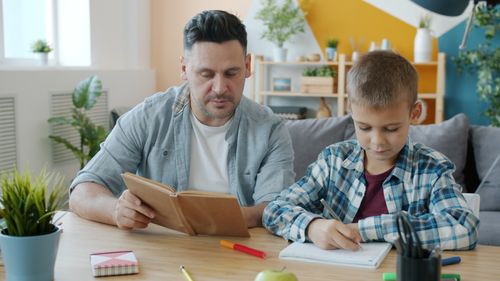 Free Father assisting his son with homework at home in a cozy setting. Stock Photo