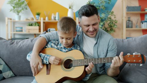 Free A heartwarming scene of a father teaching his son guitar indoors. Stock Photo
