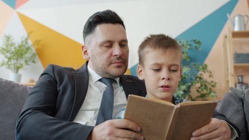 Free Father and son bonding over a book at home, sitting on a couch. Stock Photo