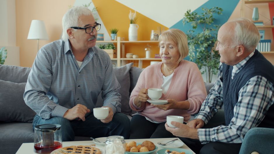 Three senior friends sharing coffee and conversation in a cozy living room setting.