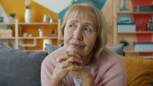 Free Pensive senior woman in cozy living room setting, lost in thought. Stock Photo