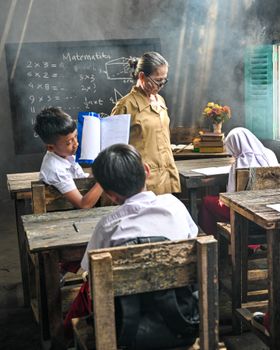 Indonesian students in a rural classroom engaged in a math lesson with a teacher.