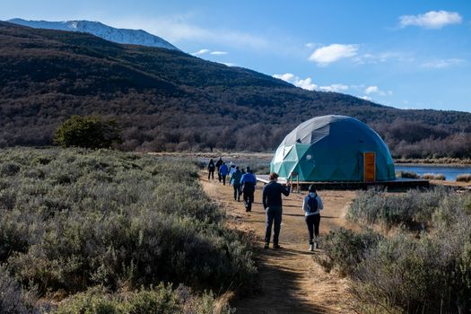 Adventurers walking towards a geodesic dome in Lapataia, Tierra del Fuego under the bright sky.