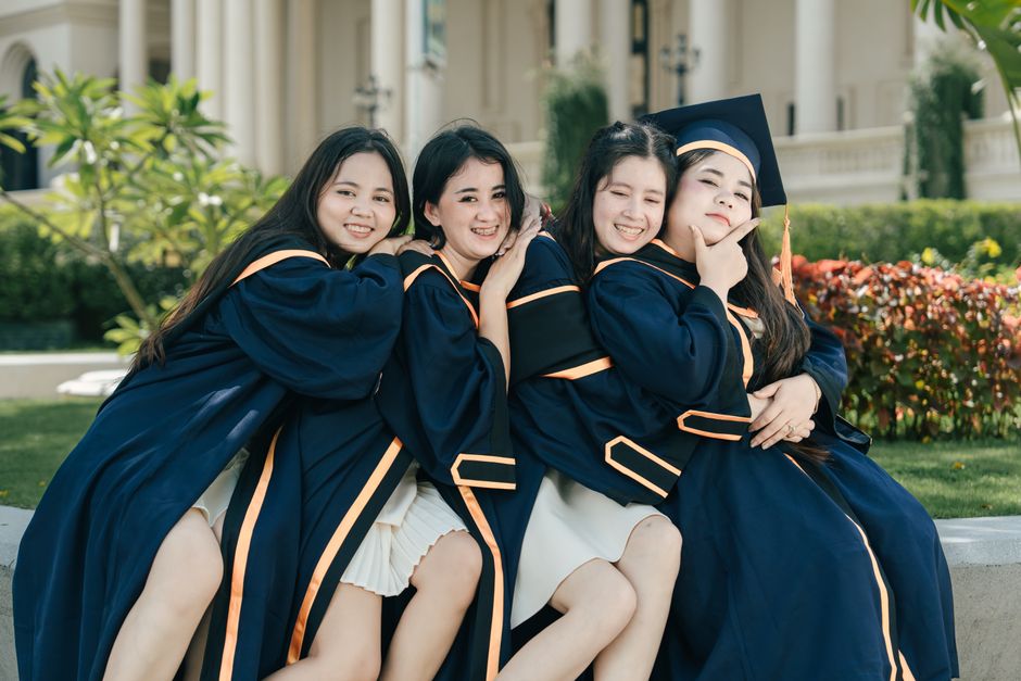 Four female graduates pose happily outdoors in caps and gowns, celebrating their academic achievements.