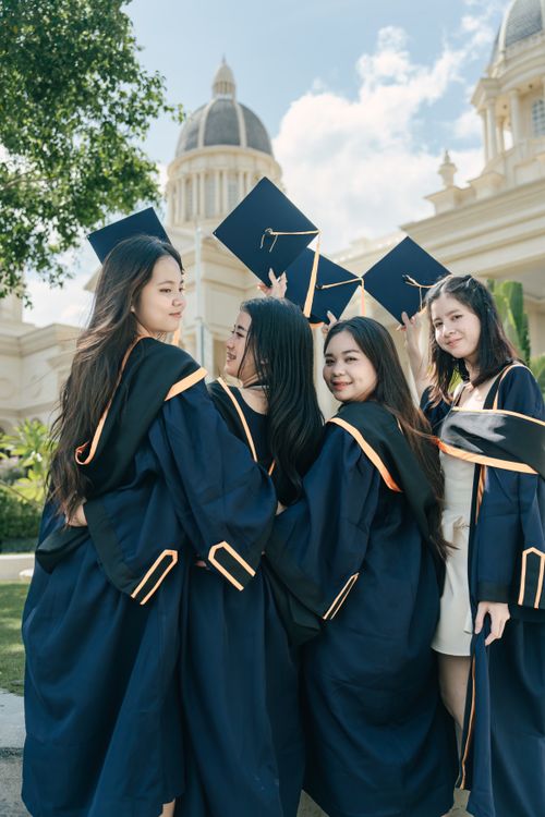 Free Group of young female graduates celebrating outdoors on a sunny day with caps in the air. Stock Photo