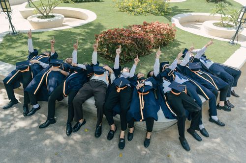 Free Graduates in caps and gowns celebrate by pointing skyward outdoors on a sunny day. Stock Photo