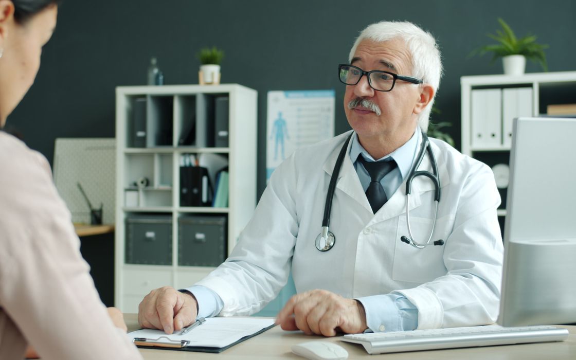 Senior doctor talking with a patient across a desk in a medical office
