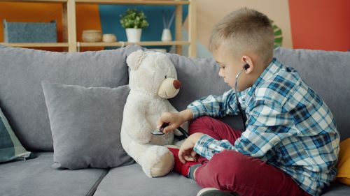 Free Young boy uses stethoscope on teddy bear, playing doctor on a couch. Stock Photo