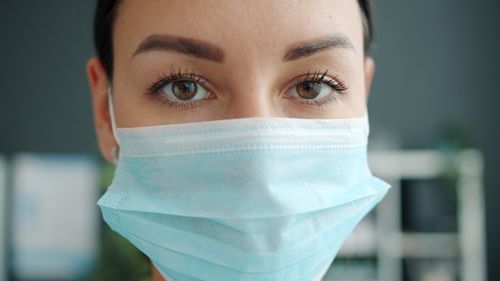 Free Close-up of a woman's eyes wearing a light blue medical face mask indoors. Stock Photo