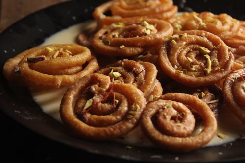 Free Close-up of crispy jalebi dessert garnished with saffron and pistachios in milk. Stock Photo