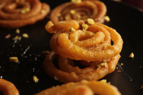 Free Delicious crispy Indian Jalebi garnished with chopped nuts on a dark plate. Stock Photo