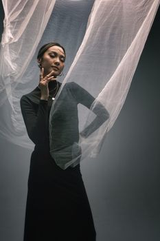 Artistic portrait of a woman in graceful pose with flowing sheer fabric, exuding elegance and mystery.