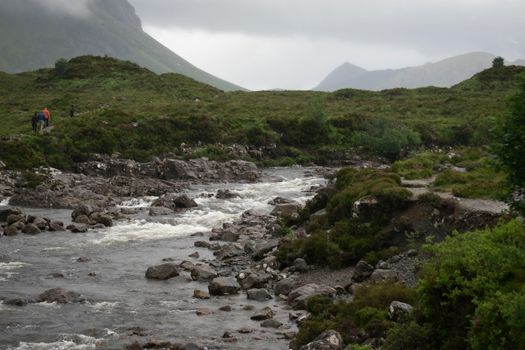A tranquil river scene with rolling green hills and hikers in the distance.