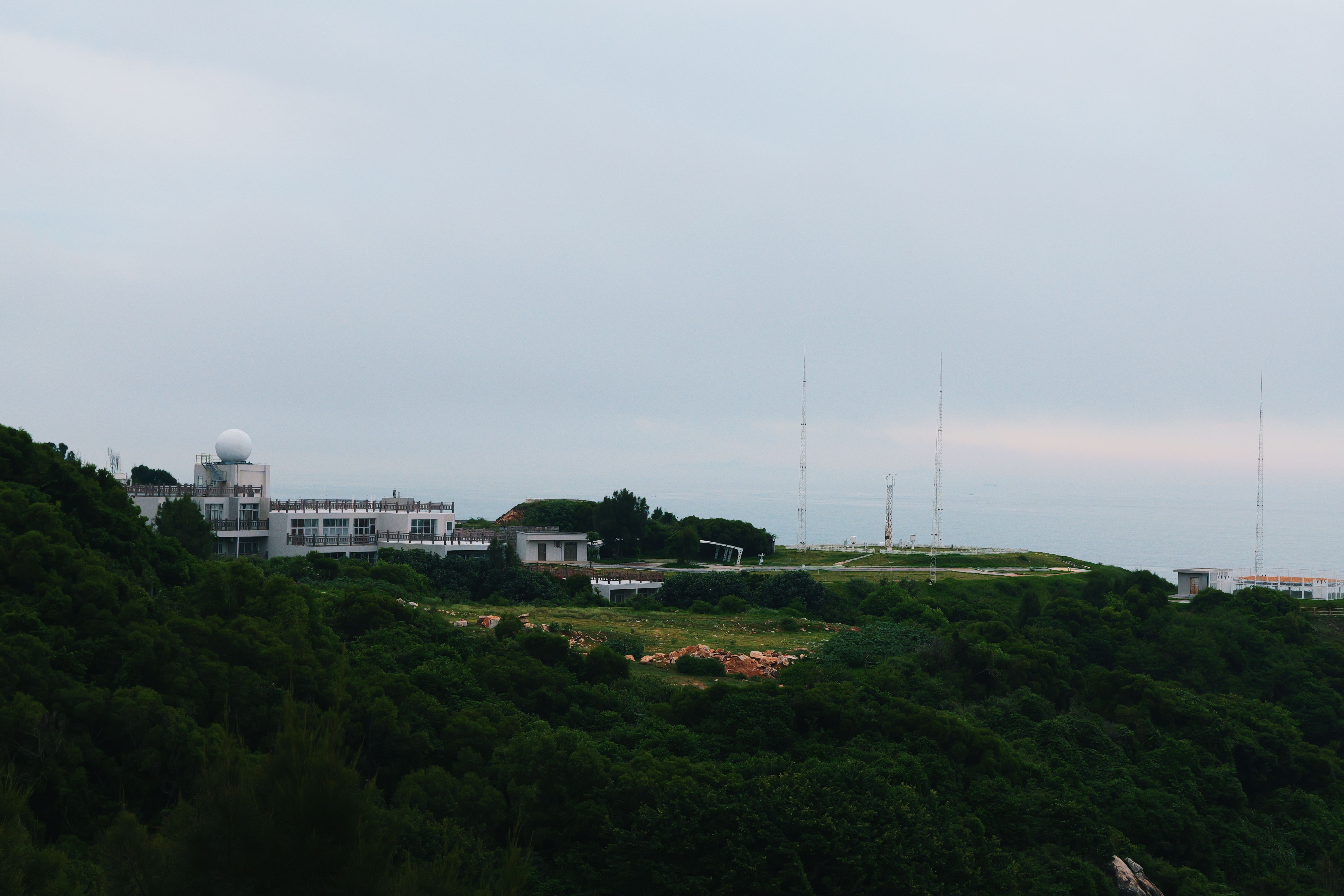 A distant radar station sits atop a lush green hill under an overcast sky.