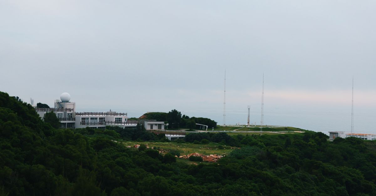 A distant radar station sits atop a lush green hill under an overcast sky.
