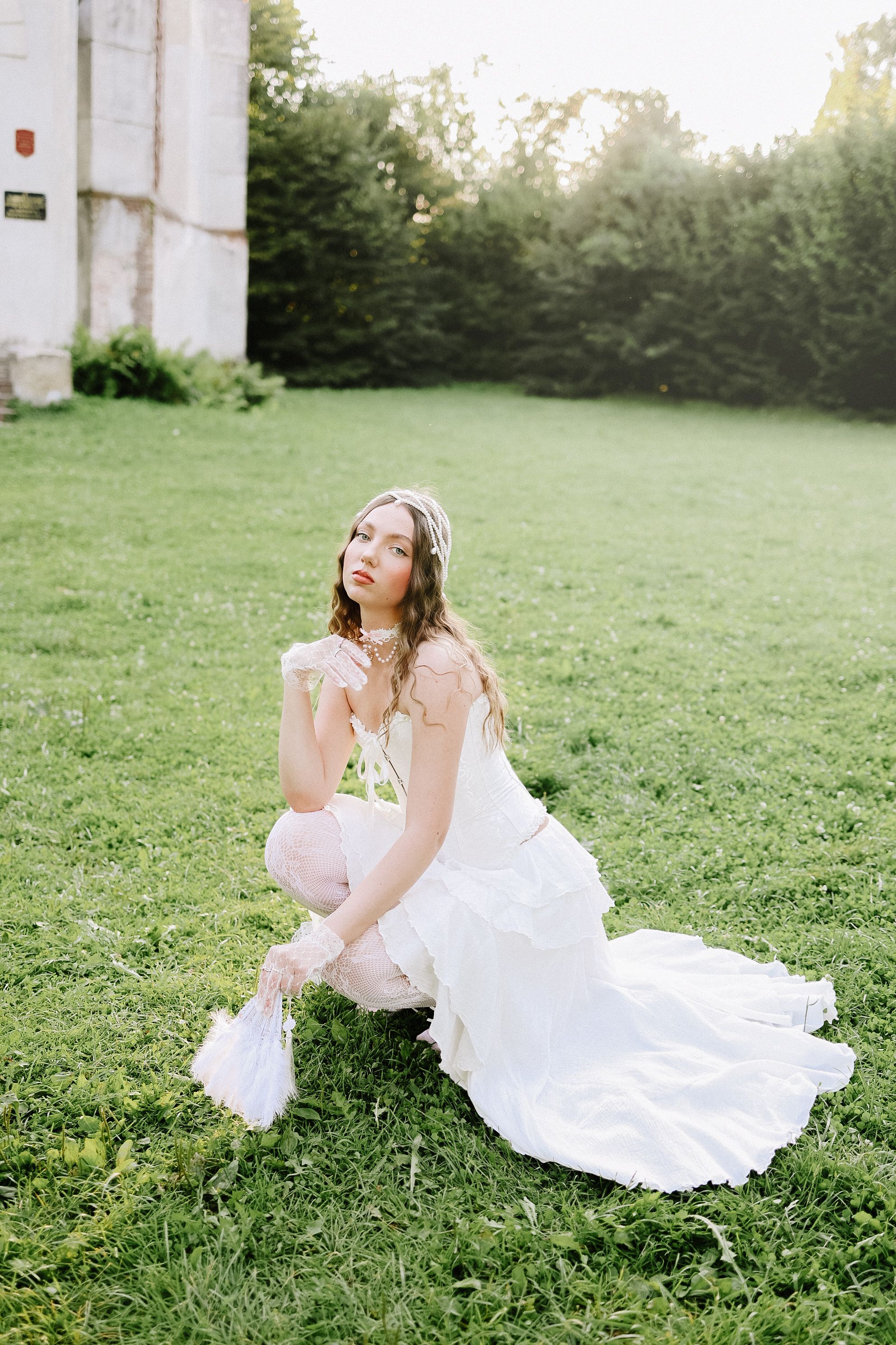 A stylish woman in a white dress poses elegantly on a grassy lawn.