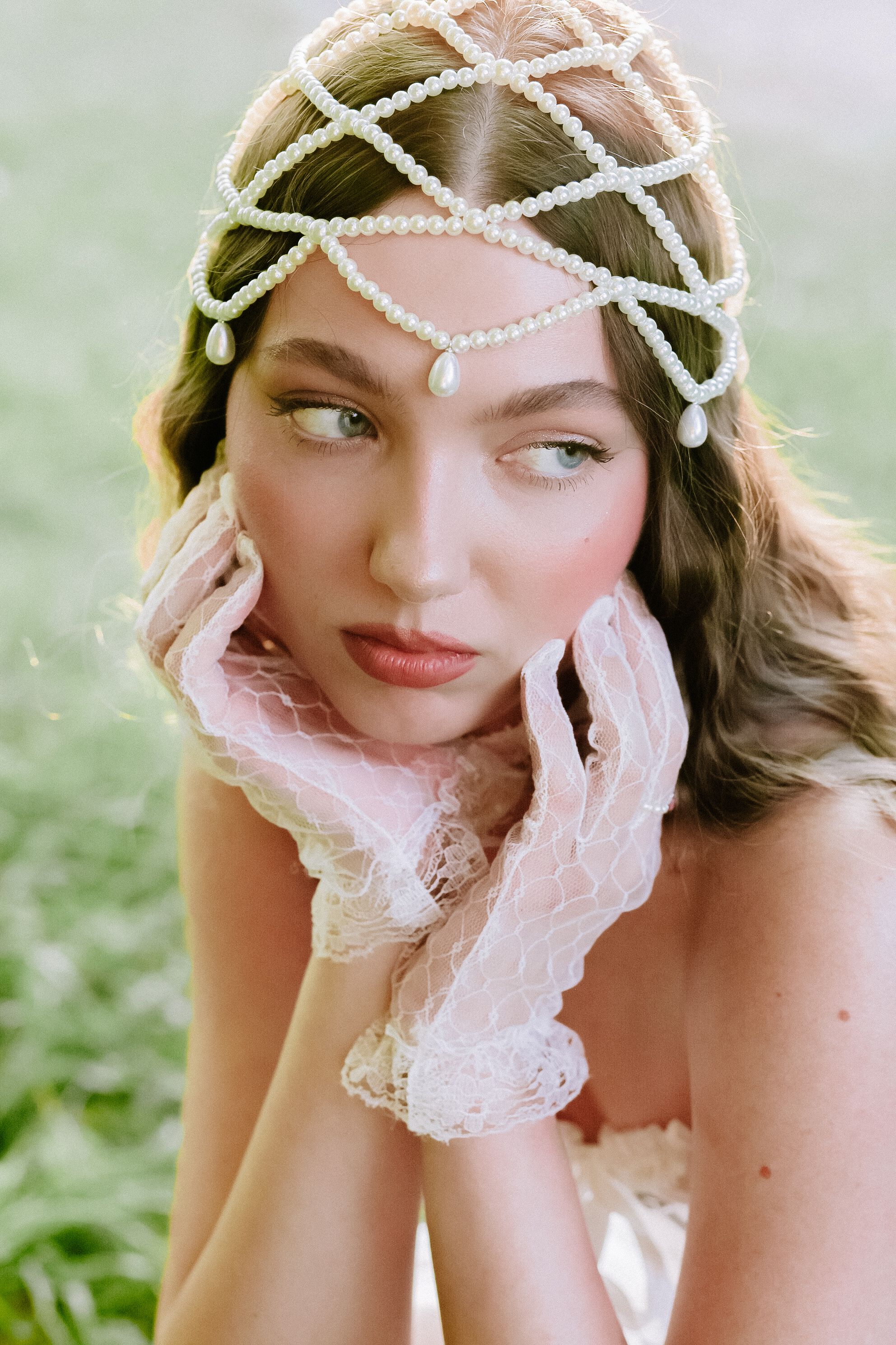Beautiful portrait of a woman wearing vintage lace gloves and a pearl headpiece outdoors.