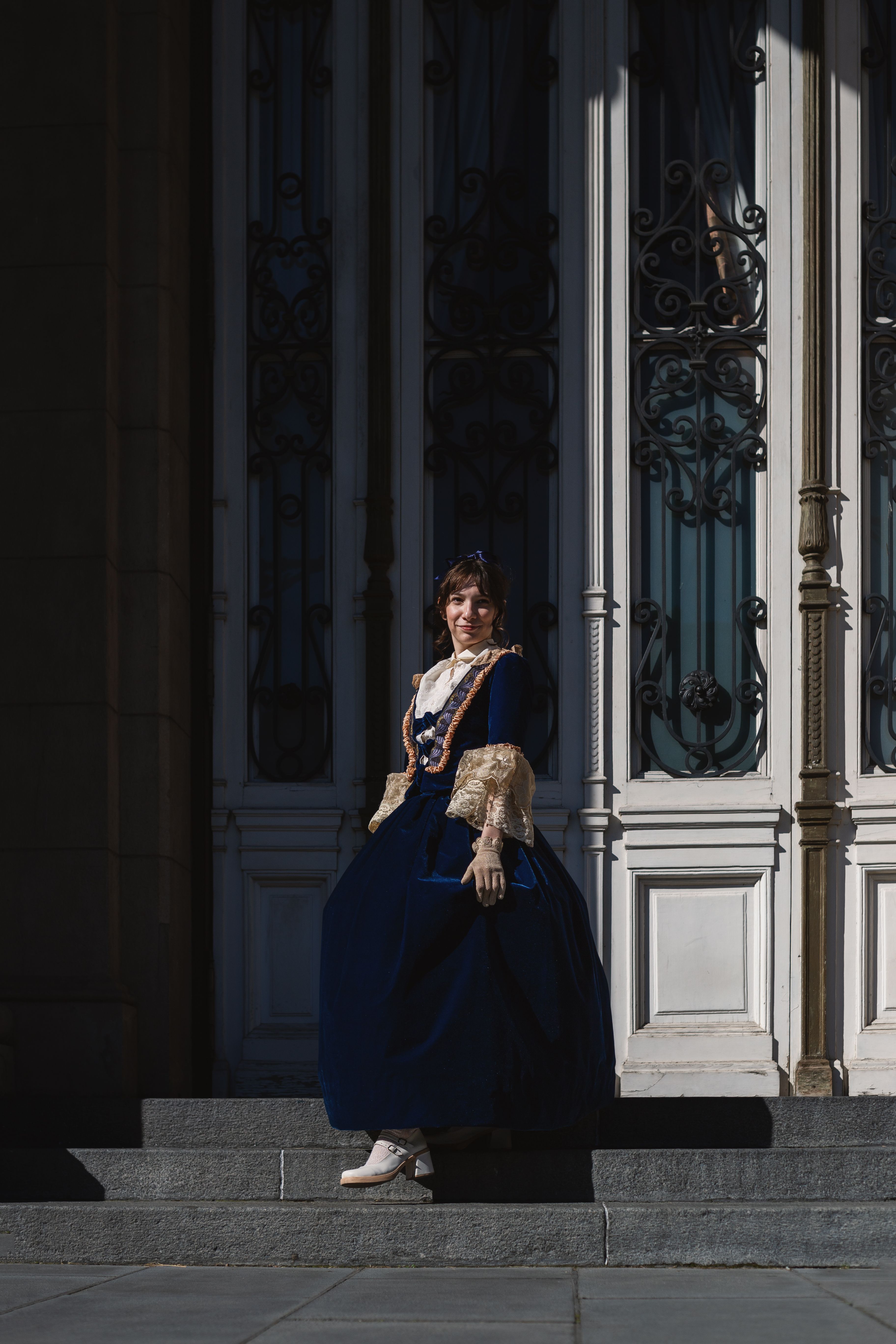 A woman in historical attire poses on the steps of a grand building in Buenos Aires.