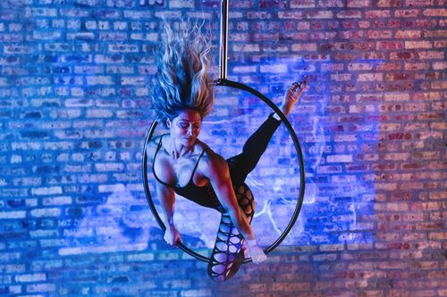 Free Aerial artist gracefully performing on a hoop, illuminated by colorful lights against a brick wall backdrop. Stock Photo