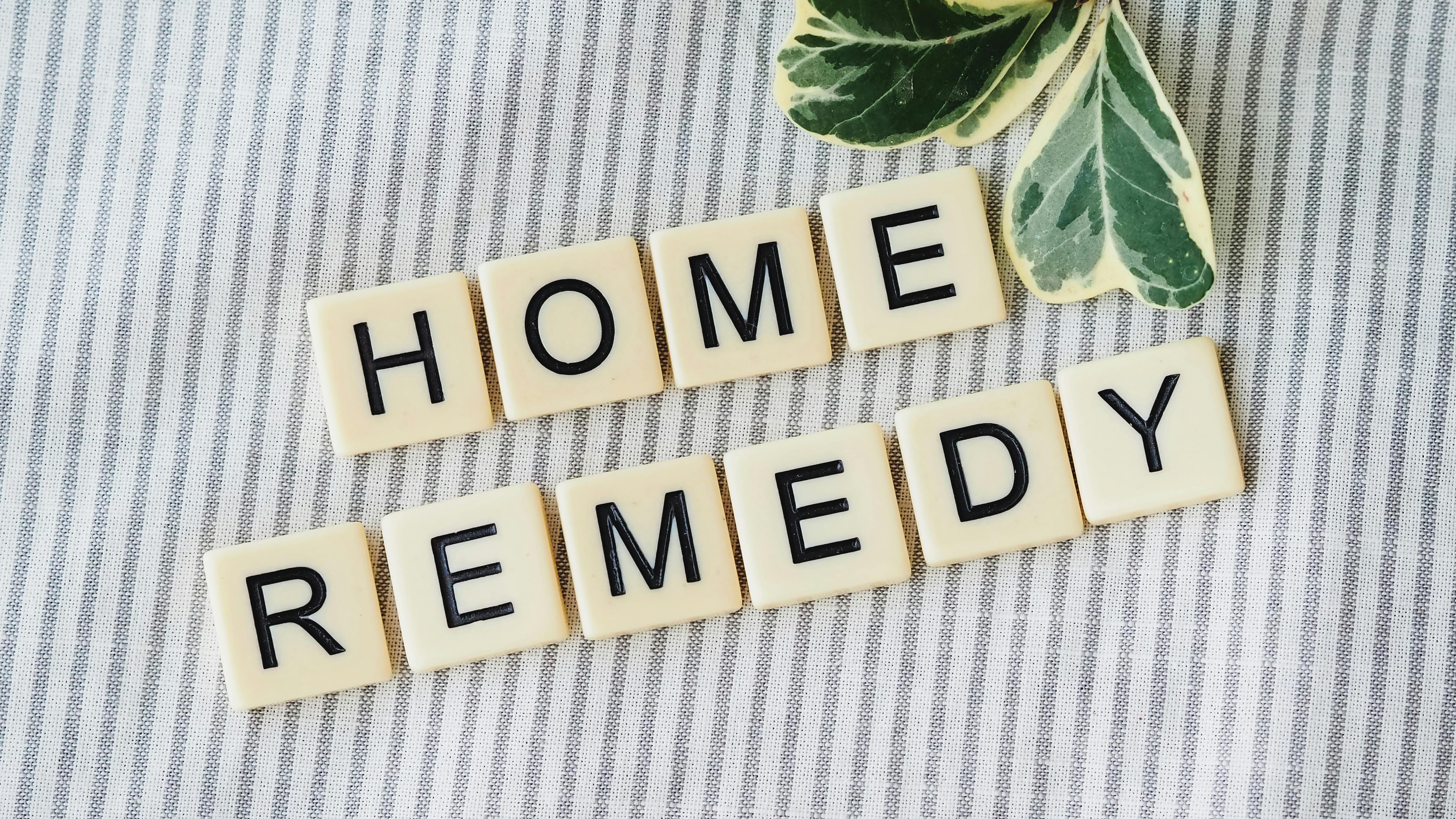 Scrabble tiles forming 'Home Remedy' with green leaves on a striped background.