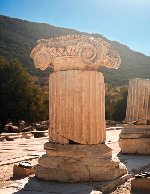 Free Close-up of an ancient Ionic column under sunlight in historic ruins with a mountainous backdrop. Stock Photo