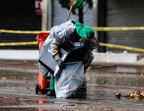 Free Street worker cleaning during rain in Pereira, Colombia, wearing rain poncho and green hat. Stock Photo