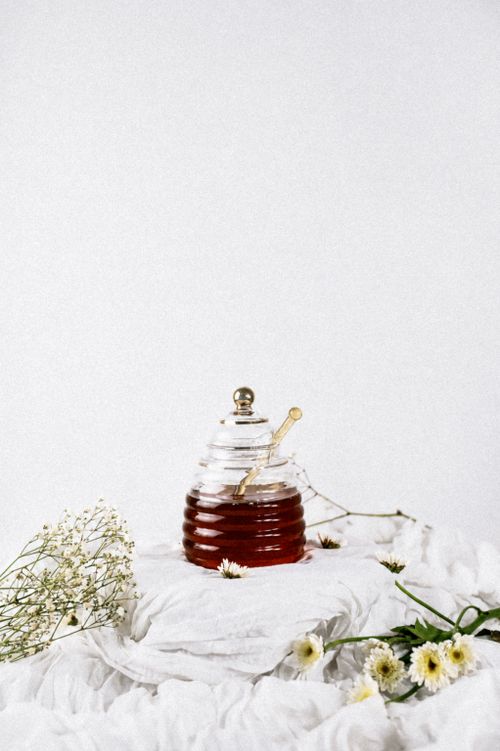 Free Glass honey jar with dipper surrounded by delicate wildflowers, perfect for kitchen decor. Stock Photo