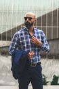 一位戴着太阳镜、身穿蓝色格子衬衫的时尚光头男子，在户外自信地摆出姿势