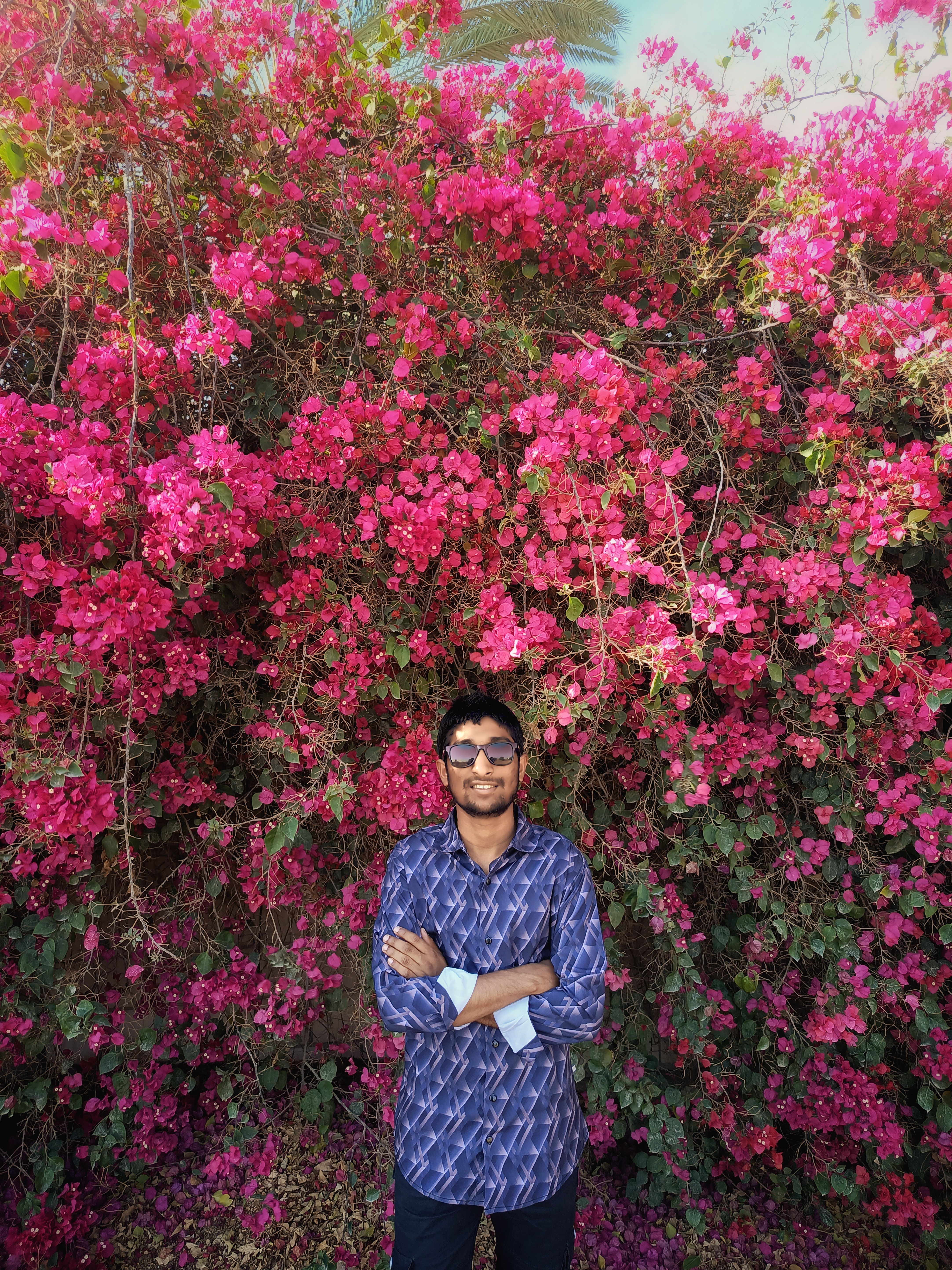 Man standing confidently in front of bright pink bougainvillea flowers, exuding a warm summer vibe.