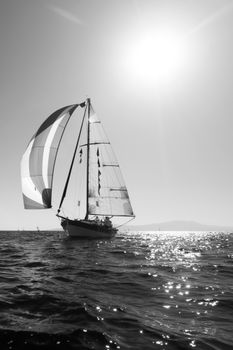 Black and white photo of a sailing boat under the bright sun reflecting on the water.