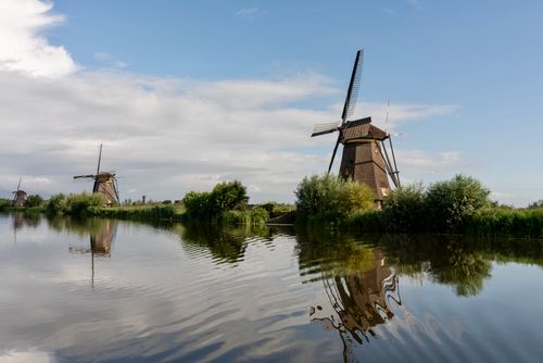 Free Picturesque view of iconic Kinderdijk windmills with reflections on a tranquil river under a clear blue sky. Stock Photo