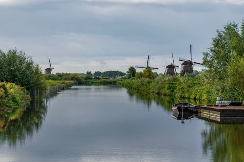 Free Serene view of iconic windmills and canal at Kinderdijk, a UNESCO heritage site, under a cloudy sky. Stock Photo