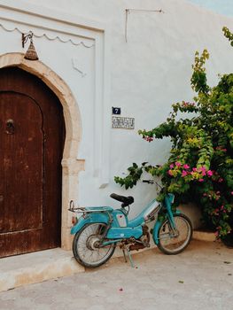 A nostalgic scene with a vintage moped leaning against a picturesque Tunisian doorway, adorned with vibrant bougainvillea.