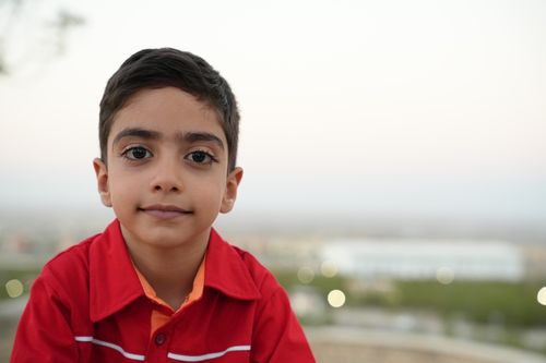 Free Close-up portrait of a young boy in a red shirt with a blurred cityscape background. Stock Photo