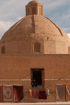 A historic domed structure in Bukhara, Uzbekistan, adorned with traditional carpets on display.